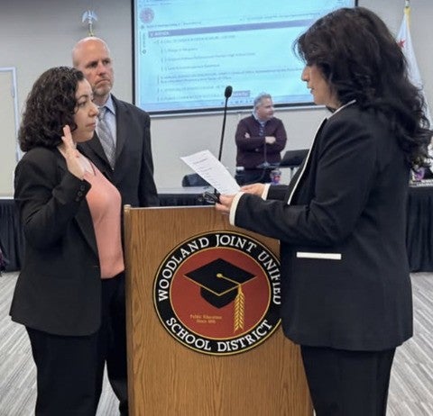 Claudia Rodriguez-Mojica stands at a podium and raises her right hand to be sworn into the school board of trustees.