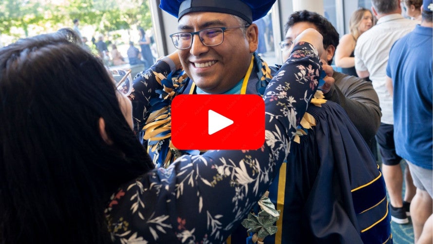 YouTube title image of a doctoral graduate's family placing a lei on his shoulders.