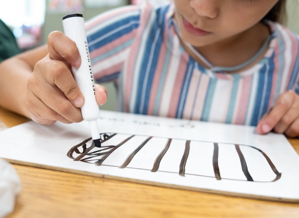 A young girl draws lines on a hand-held white board.