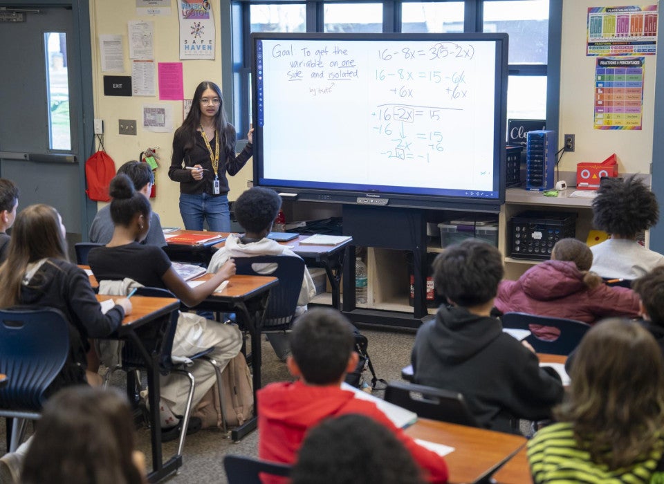 A teacher stands at the front of the classroom and writes math equations on the board.