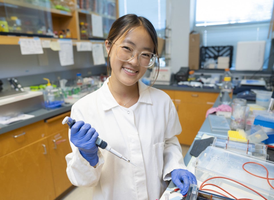 A student holds a pipette and smiles for the camera.