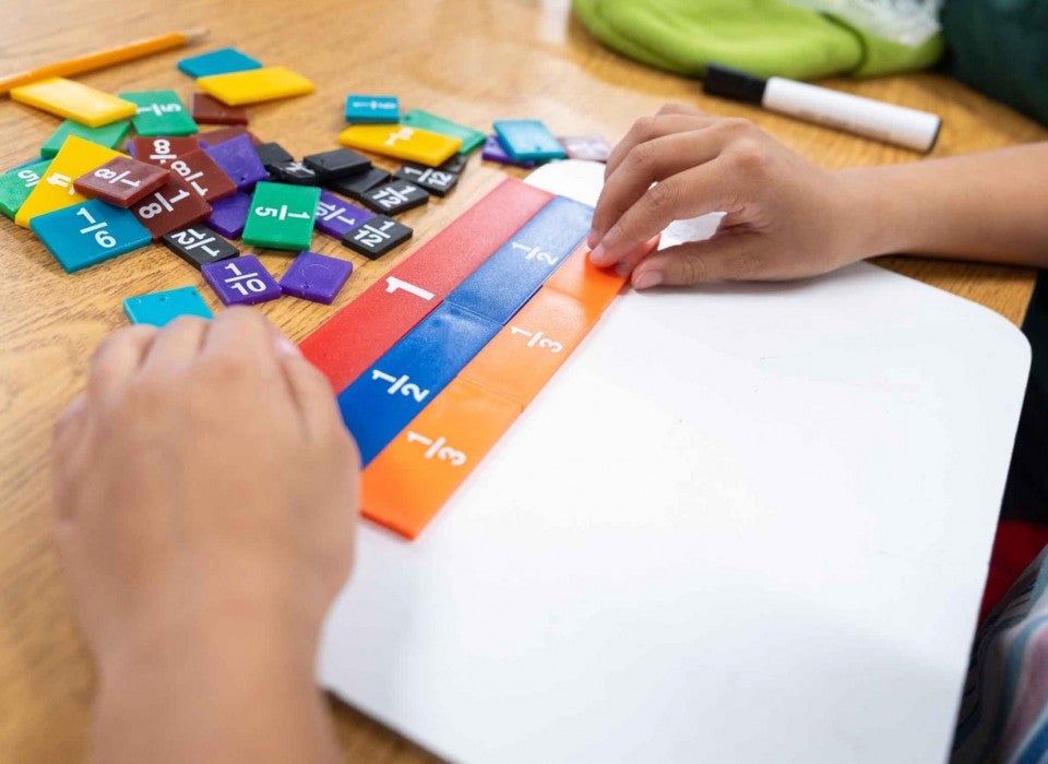 Closeup of a student's hands putting together colored tiles with math equations on them.
