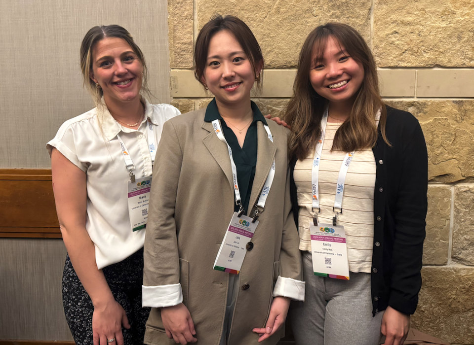 Three women stand together, wearing lanyards and professional clothing.