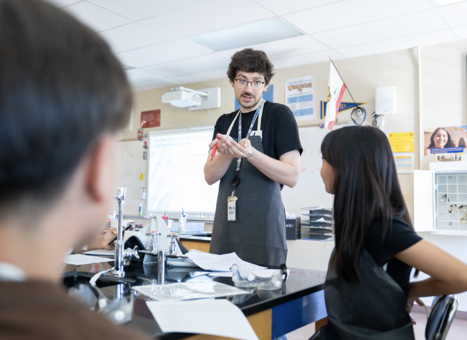 A science teachers addresses a group of students seated in front of him