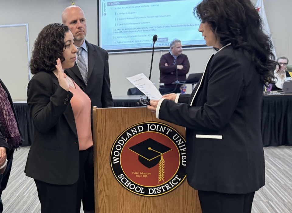 Claudia Rodriguez-Mojica stands in front of a podium and raises her right hand to be sworn into the board of trustees.