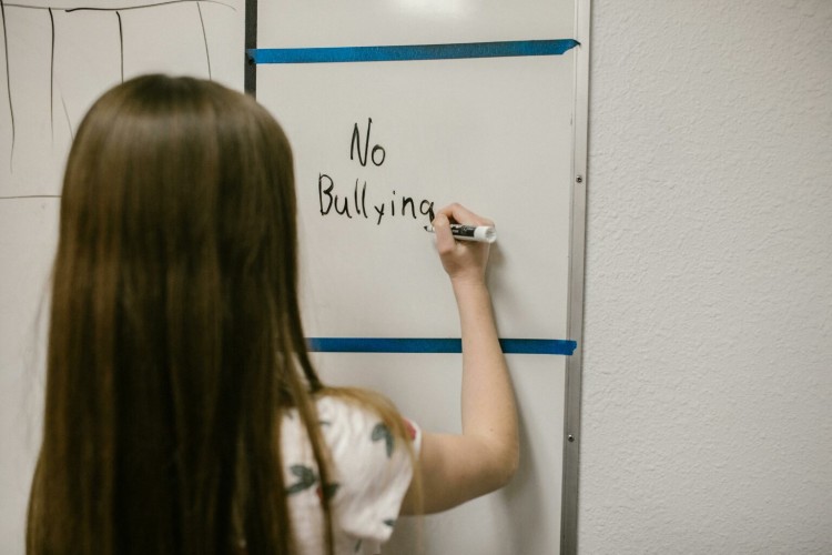 A young girl faces away from the camera and writes "no bullying" onto a white board.