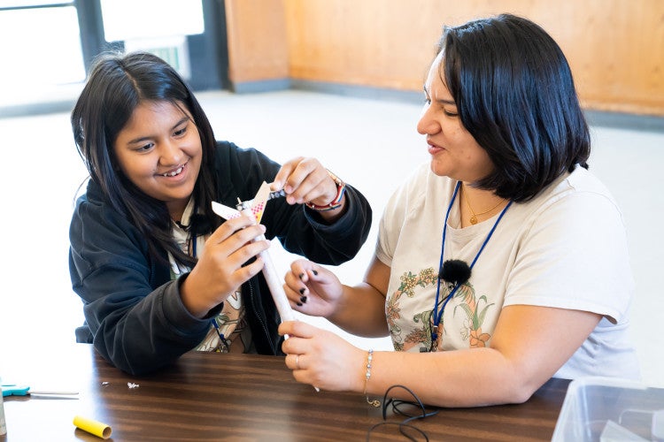 Daughter and mother smiling as they assemble a rocket in a school cafeteria