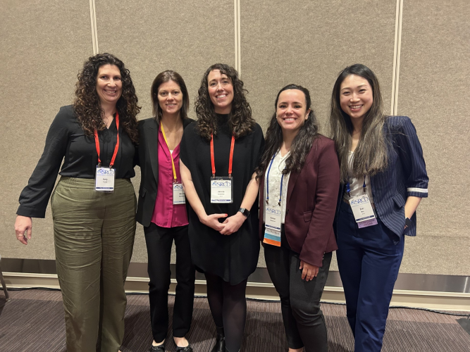 Five women stand together wearing lanyards and professional outfits.
