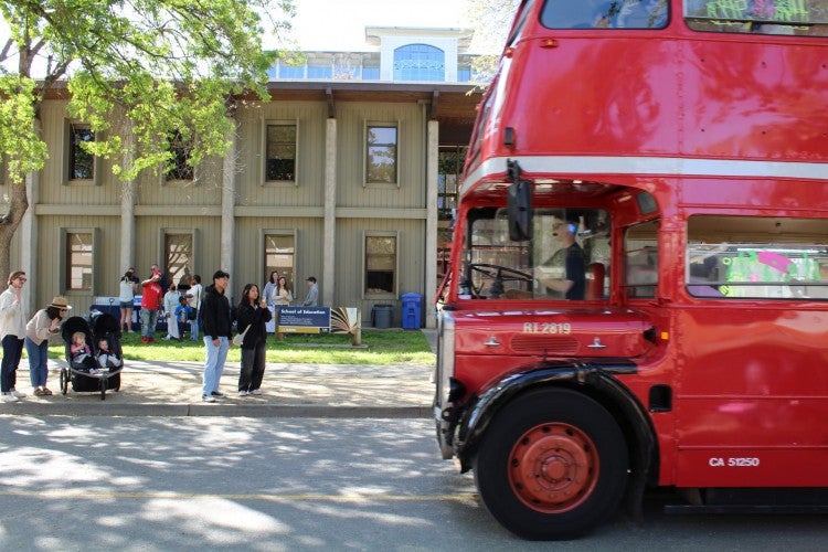 A red double-decker bus drives by the outside of the School of Education building.