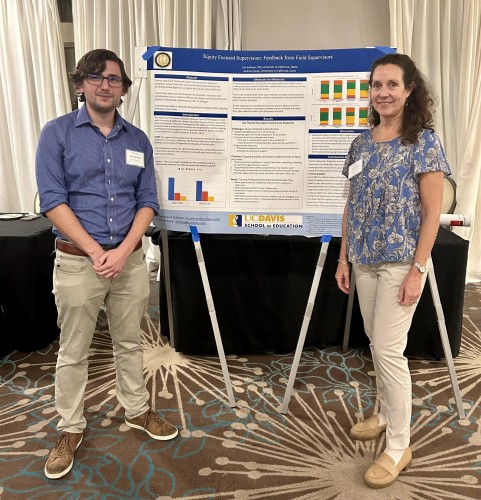 Man and woman stand on either side of a poster board propped on an easel