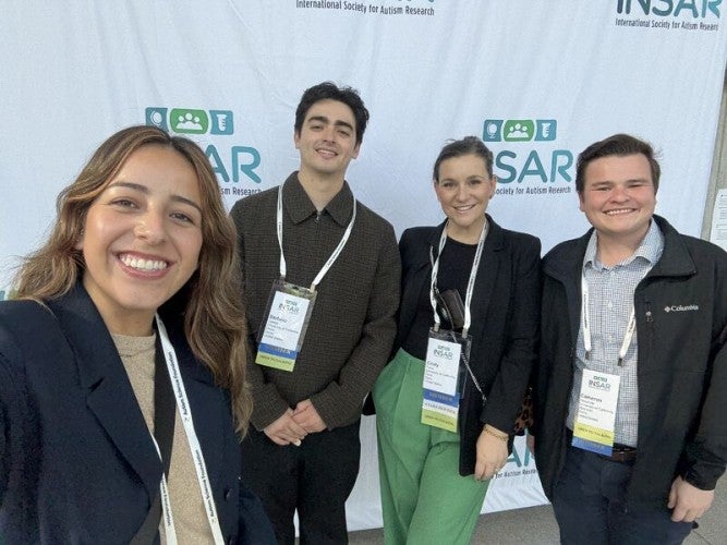 A group of four PhD students pose together in front of a photo screen background with "INSAR" printed across it.