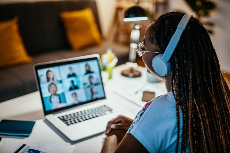 A woman wearing headphones addresses a group of people on a laptop screen.