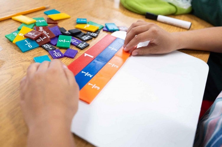 A closeup of a child's hands as they move colored tiles around on their desk.