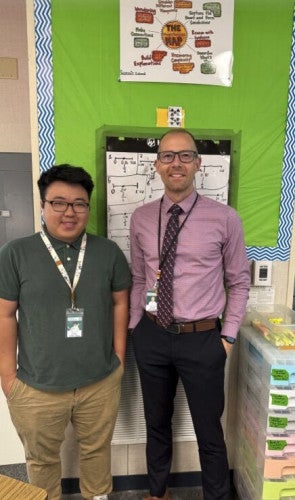 Bryan Tan and Matthew Tealdi stand against a classroom wall and smile.