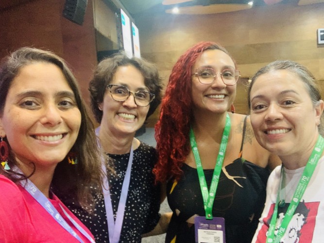 Four women wearing name tags and badges pose together for a photo