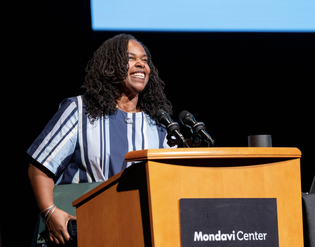 Renée Watson stands at a podium and smiles while speaking into a microphone. A sign on the podium reads "Mondavi Center."